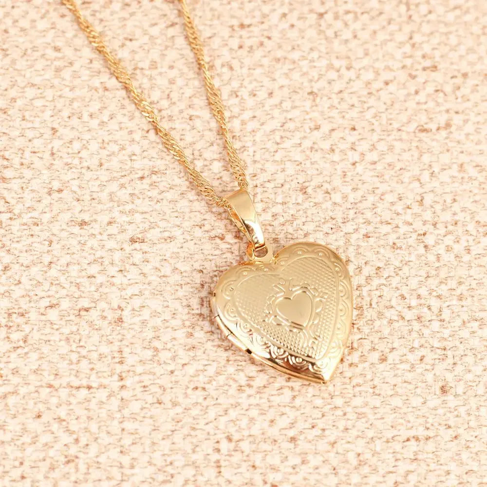 Colar dourado com pingente em formato de coração com detalhes gravados sobre tecido bege texturizado