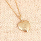 Colar dourado com pingente em formato de coração com detalhes gravados sobre tecido bege texturizado