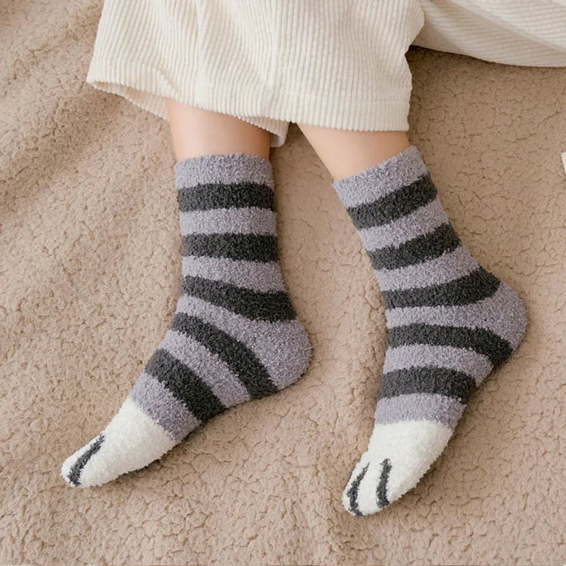Pés com meias felpudas listradas cinza e preto com ponta branca, sobre cobertor bege texturizado