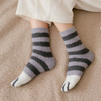 Pés com meias felpudas listradas cinza e preto com ponta branca, sobre cobertor bege texturizado