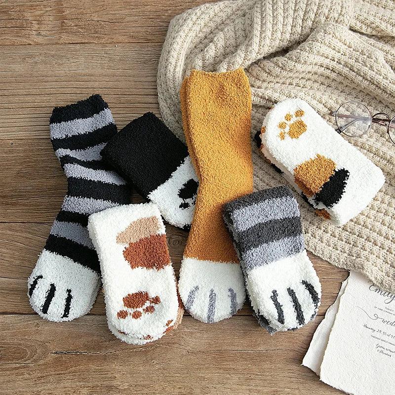 Meias felpudas de inverno com estampas de patas de gato, cores variadas, sobre superfície de madeira