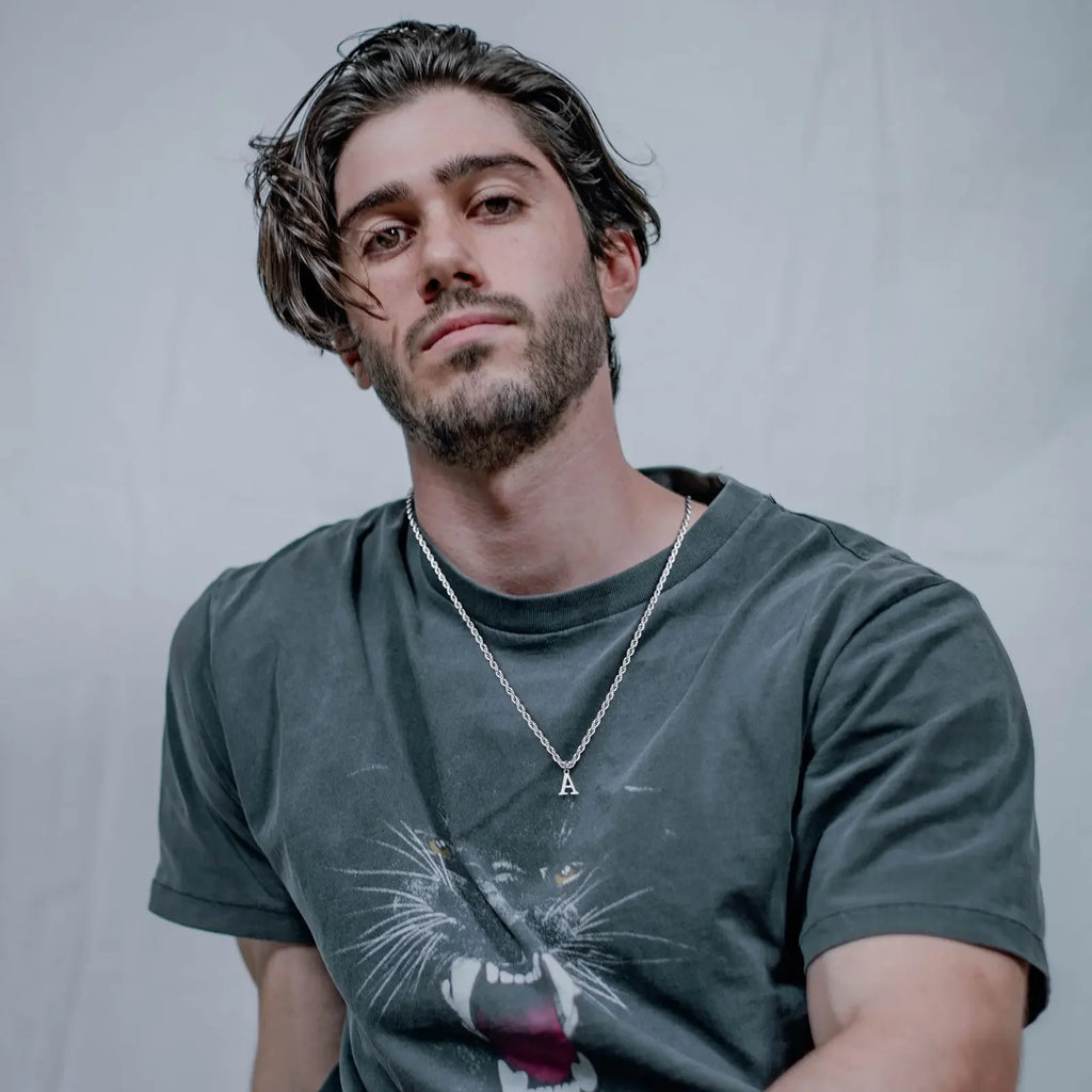 Homem com colar prateado com letra A e camiseta gola careca com estampa de pantera